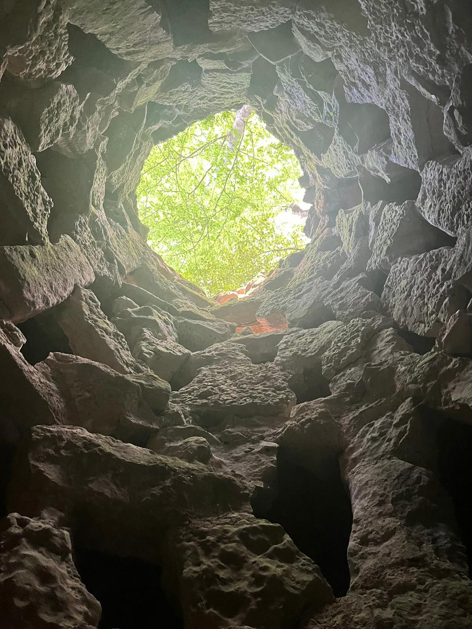 Abertura circular entre pedras revelando o céu e as árvores